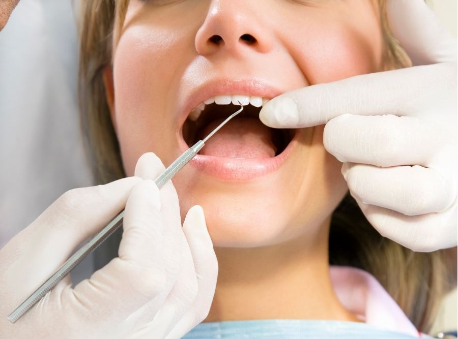 Orthodontist wearing white gloves examining a patient’s teeth during an orthodontic visit, close-up of mouth and dental instruments.