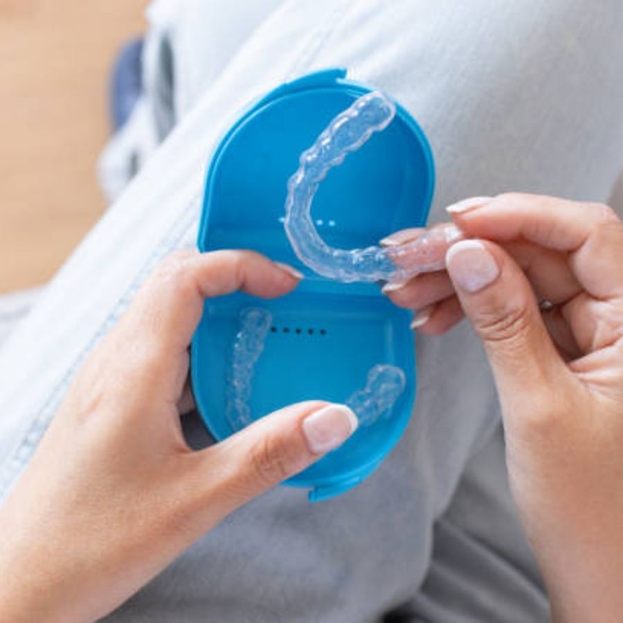 A patient holding clear plastic aligners over a blue storage case, highlighting modern orthodontic care options in Bath, SC.