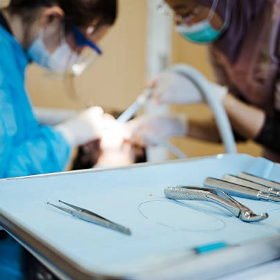 Dental surgical tools on a sterile tray in the foreground with orthodontists performing a procedure in a Hephzibah, GA clinic