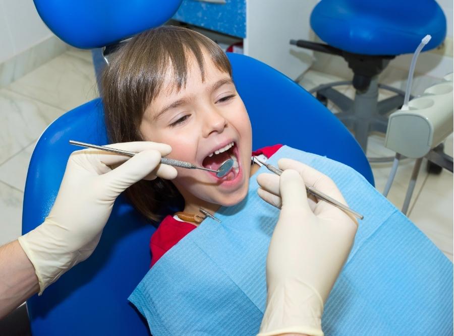 A young girl sitting in a blue dental chair receiving a pediatric orthodontic checkup with a dental mirror in Harlem, GA